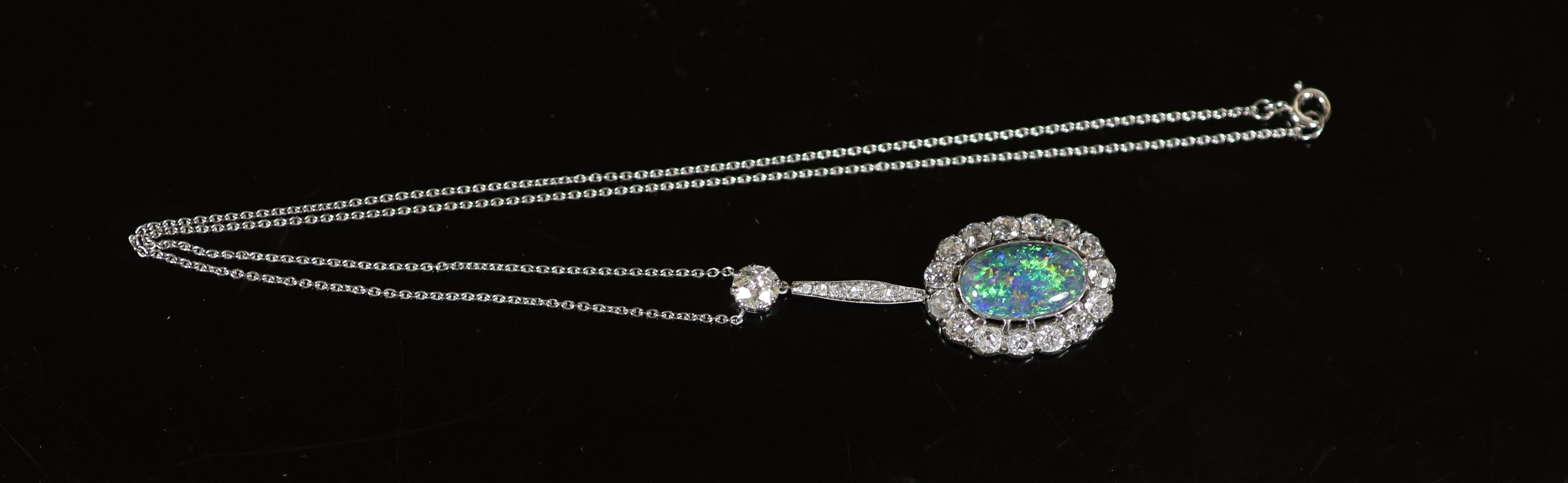 An early 20th century white gold, oval black opal and diamond cluster set drop pendant necklace